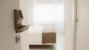 Ein modernes Hotelzimmer mit einem elektronischen Türschloss, einem Bett mit brauner Decke und einem Fenster mit Jalousien.