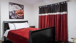 Une chambre avec un cadre de lit noir, une literie rouge et un tableau représentant des fleurs accroché au mur.