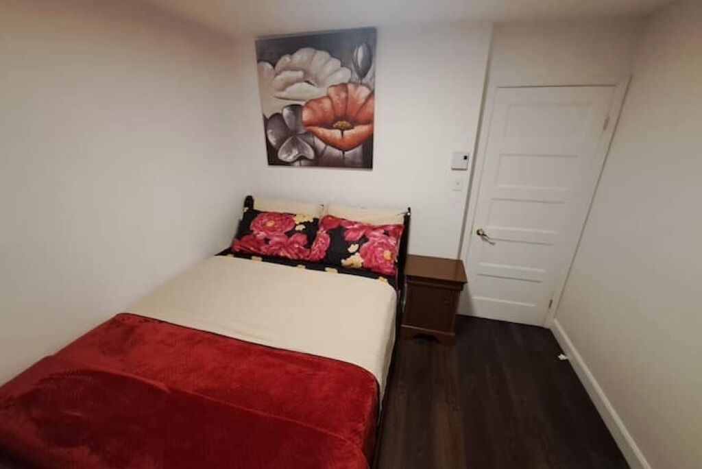 Un dormitori amb un llit, una taula de nit, una porta i un quadre penjat a la paret.