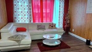 Un salon avec un canapé blanc, des coussins rouges, une table basse en verre et des rideaux à motifs.