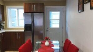 Une cuisine compacte comprenant un réfrigérateur, une table à manger avec des chaises rouges et un vase rempli de fleurs.