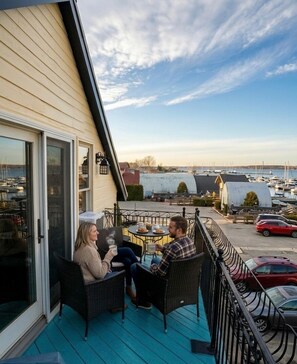 Un balcon agrémenté de meubles en osier, une vue sur un port de plaisance et un bâtiment doté d’un toit en pente.