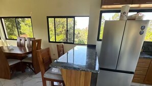 Una cocina con piso de mármol, sillas de madera, un refrigerador de acero inoxidable y ventanas amplias.