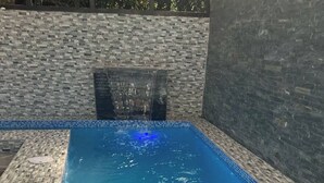 Una bañera de hidromasaje rectangular con borde de azulejos, rodeada por un muro de piedra.