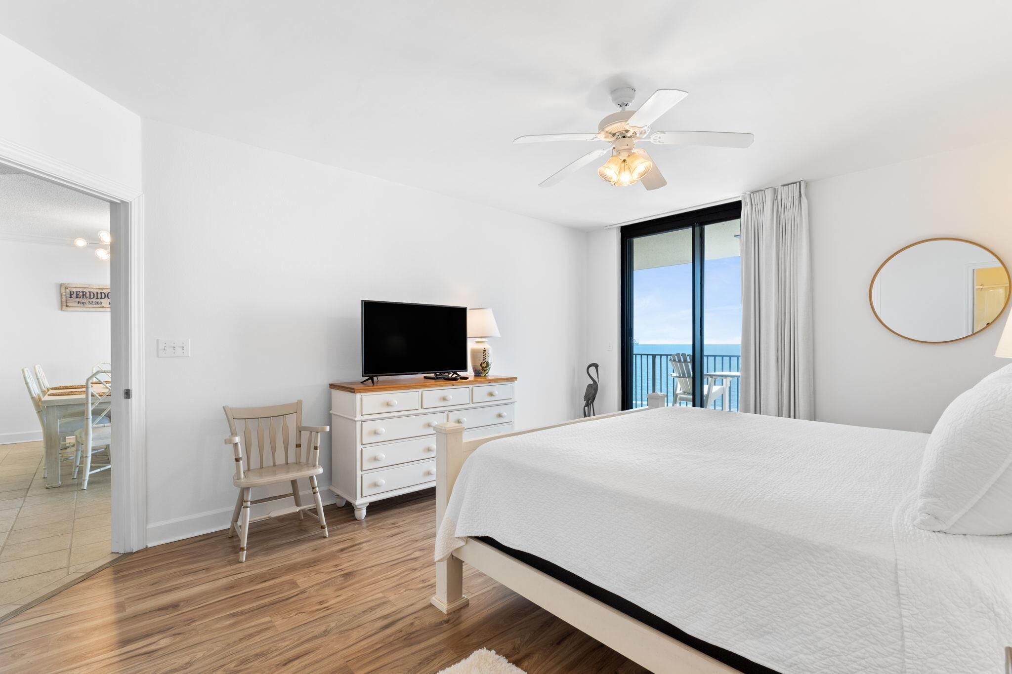 Ein Schlafzimmer mit einem Bett, einem Fernseher auf einer Kommode, einem Deckenventilator und Blick ins Freie.