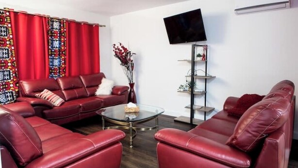Ein Wohnzimmer mit roten Ledersofas, einem Glastisch und einem an der Wand befestigten Flachbildfernseher.