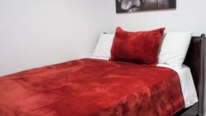 Ein Bett mit roter Decke, weißen Kissen, einem dunklen Kopfteil und einem gerahmten Bild an der Wand.