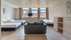 Una habitación de hotel moderna con tres camas, un sofá, una televisión y un ventanal con vistas a la ciudad.