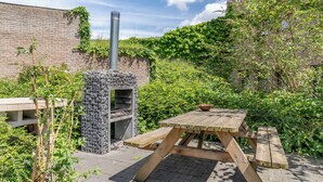 Un patio al aire libre con un horno de ladrillo, una mesa de picnic de madera y un muro de ladrillo con plantas.