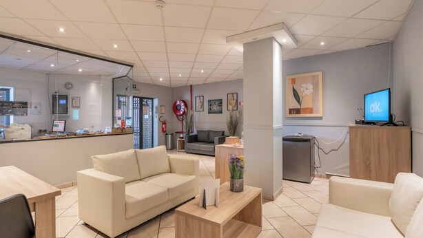 Un área de recepción moderna con un sofá color beige, una mesa de centro de madera y un televisor sobre un mueble de madera.