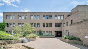 Un edificio moderno con patio interior, fachada de ladrillo, amplias ventanas y algo de vegetación.
