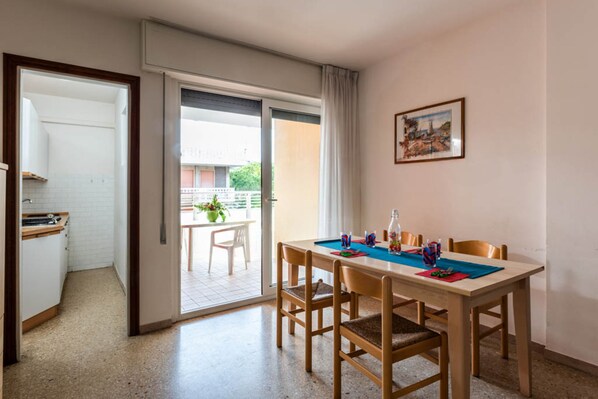 A dining area with a table set for four, a kitchen area with a sink and countertop, and a sliding glass door leading to an outdoor balcony.