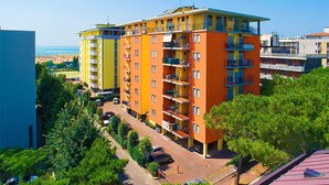 A multi-story residential building with balconies, a parking area, and a view of the beach. - Comfortable Apartment in Bibione Spiaggia (San Michele al Tagliamento)
