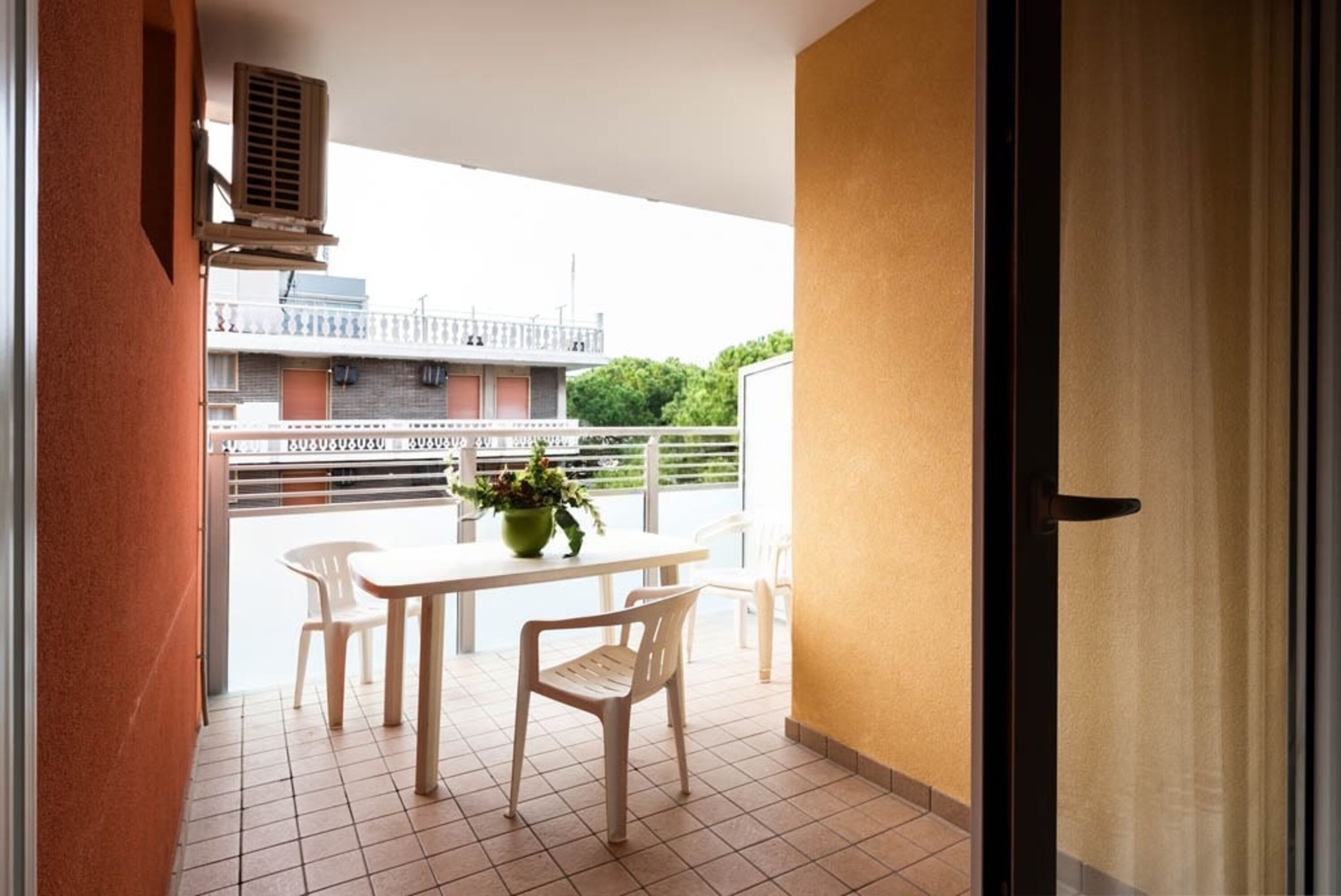 A balcony with a table and chairs, a potted plant, and a view of buildings and greenery.