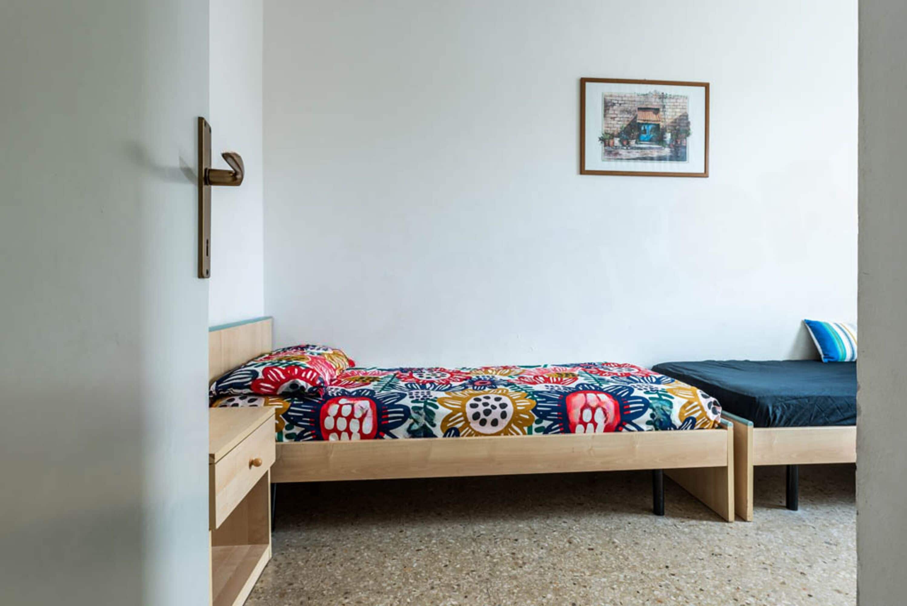 A bedroom with a bed, a nightstand, a drawer, a door handle, and a framed picture on the wall.