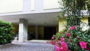 A covered parking area with bicycles, a paved walkway, and blooming pink flowers. - Comfortable Apartment in Bibione Spiaggia (San Michele al Tagliamento)