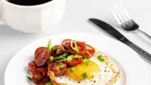 A breakfast plate with a fried egg, tomatoes, and greens, accompanied by a cup of coffee. - Rio By Glitz Hotels (Mumbai)