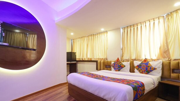 A hotel room with a large bed, a round mirror, a TV, and curtains. - Rio By Glitz Hotels (Mumbai)