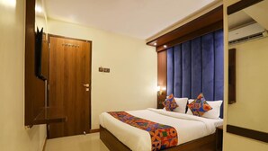 A hotel room with a wooden bed, a blue upholstered headboard, and a television mounted on the wall. - Rio By Glitz Hotels (Mumbai)