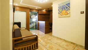A hotel hallway with a reception desk, a wooden bench, and a painting on the wall. - Rio By Glitz Hotels (Mumbai)