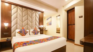 A hotel room with a large bed, a wooden headboard, a bedside table with a lamp, and a door. - Rio By Glitz Hotels (Mumbai)