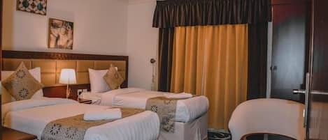 A hotel room with two beds, a sitting area with a chair and a small table, and a large window with curtains.