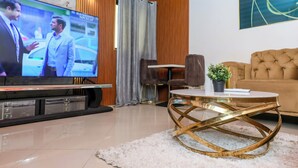 A modern living room with a flat-screen TV, a tufted sofa, a round coffee table, and a potted plant. - T-Square Residence Makepe (Douala)