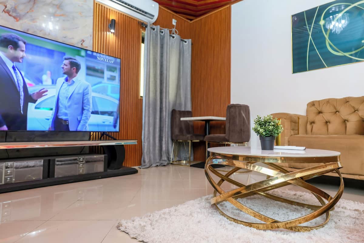 A modern living room with a flat-screen TV, a tufted sofa, a round coffee table, and a potted plant.