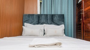 A neatly made bed with white linens and pillows, a dark upholstered headboard, and a wooden panel wall. - T-Square Residence Makepe (Douala)