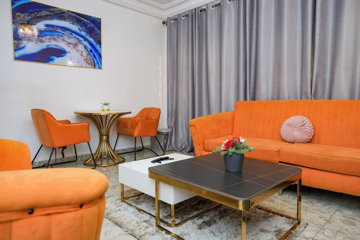 A modern living room with an orange sofa, two orange chairs, a white coffee table, and a small table with a plant.