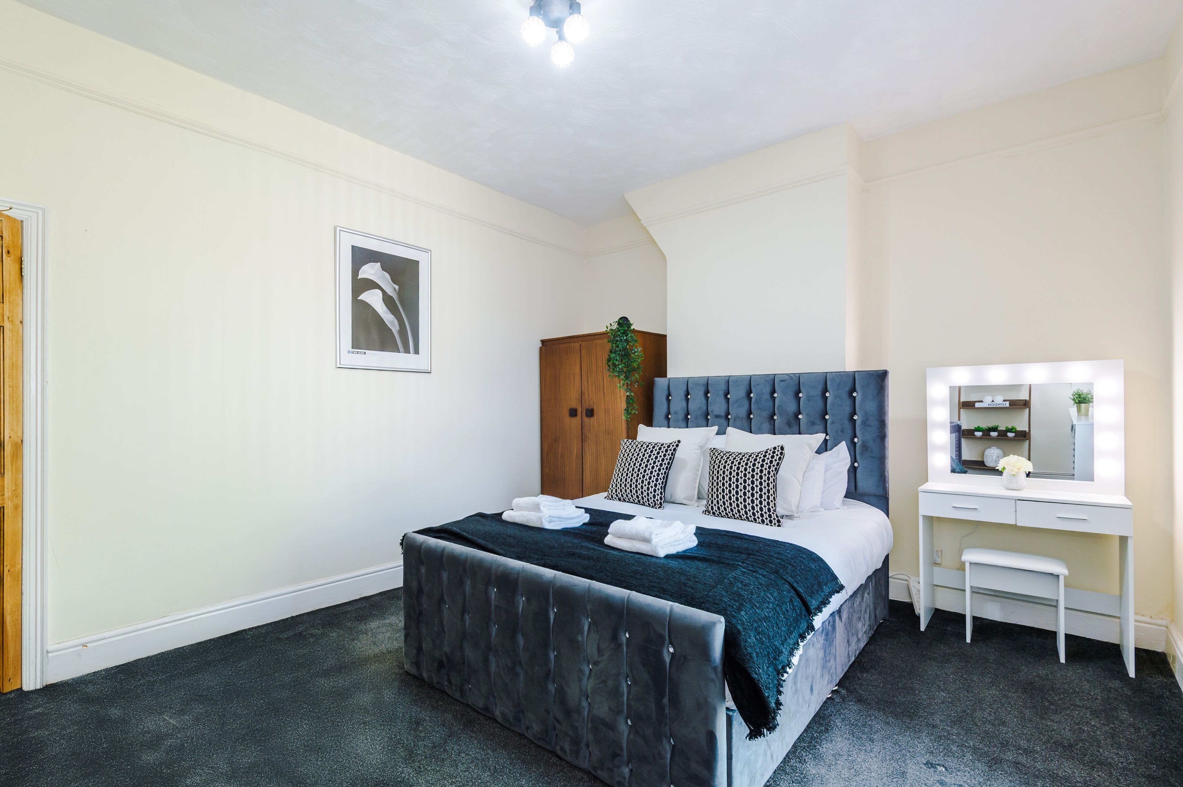 A bedroom with a bed, a vanity with a mirror, and a wooden wardrobe.