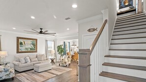 A spacious living room with a large sofa, a dining area, and a staircase with a wooden railing. - 1st Tier 3BR Home w/ Pools, Golf Cart & Beach (Port St. Joe)