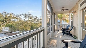 A covered porch with a ceiling fan, two chairs, and a view of trees and a building in the background. - 1st Tier 3BR Home w/ Pools, Golf Cart & Beach (Port St. Joe)