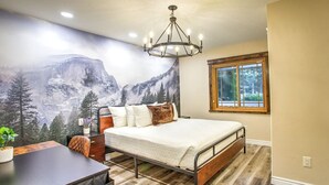 Un dormitorio con cama, escritorio, silla, ventana y un mural de un paisaje montañoso.