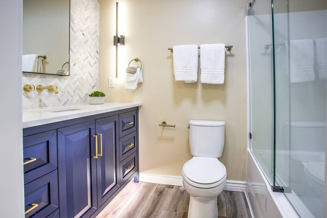 A modern bathroom with a dark blue vanity, white toilet, and a glass shower enclosure.