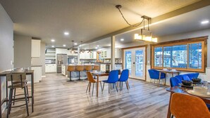A spacious kitchen with modern appliances, a dining area with blue chairs, and a large window providing a view of the outdoors.