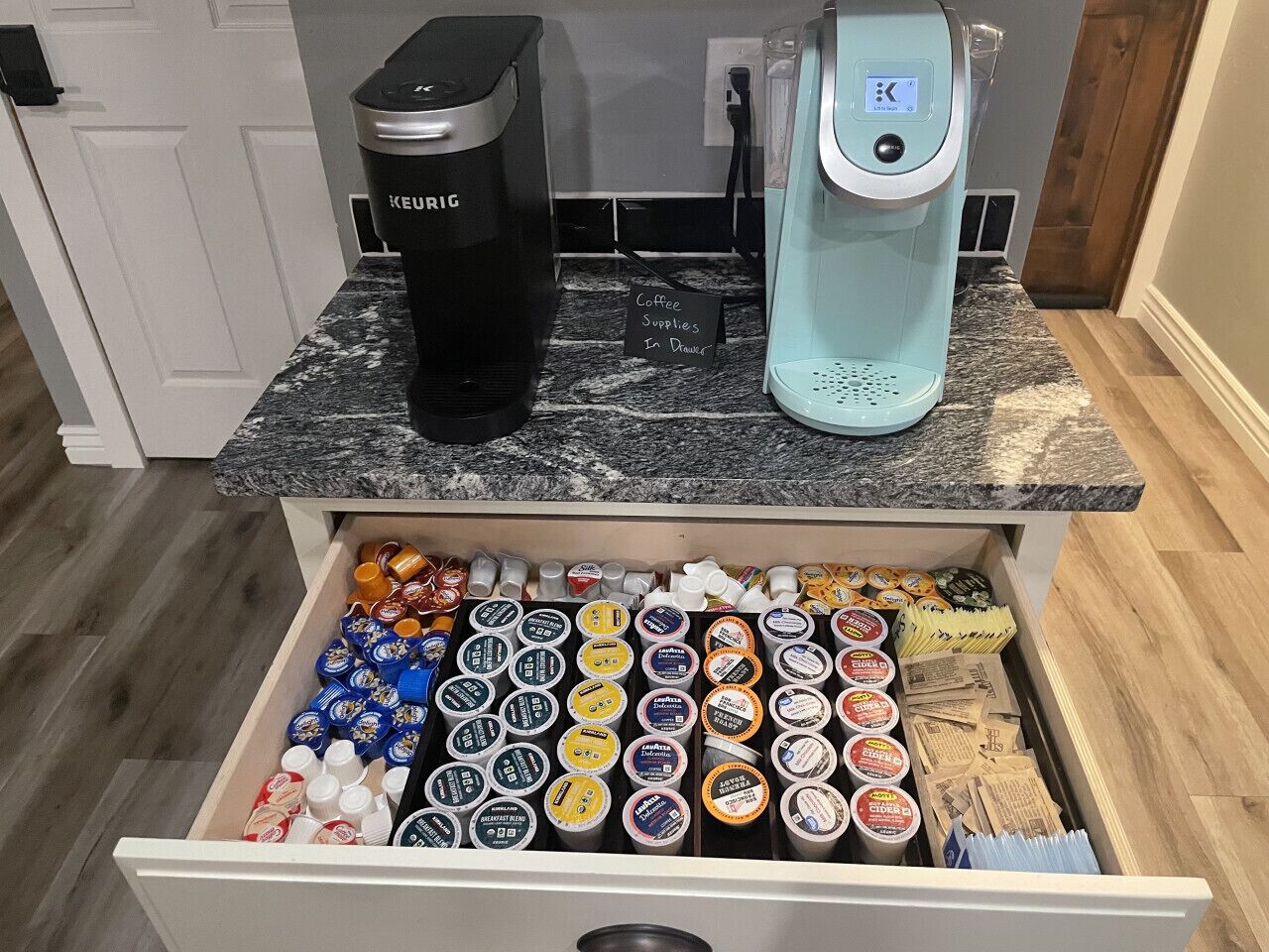 A drawer filled with coffee pods and a Keurig coffee maker on a kitchen counter.