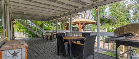An outdoor patio with a wooden deck, a table with chairs, and a grill.