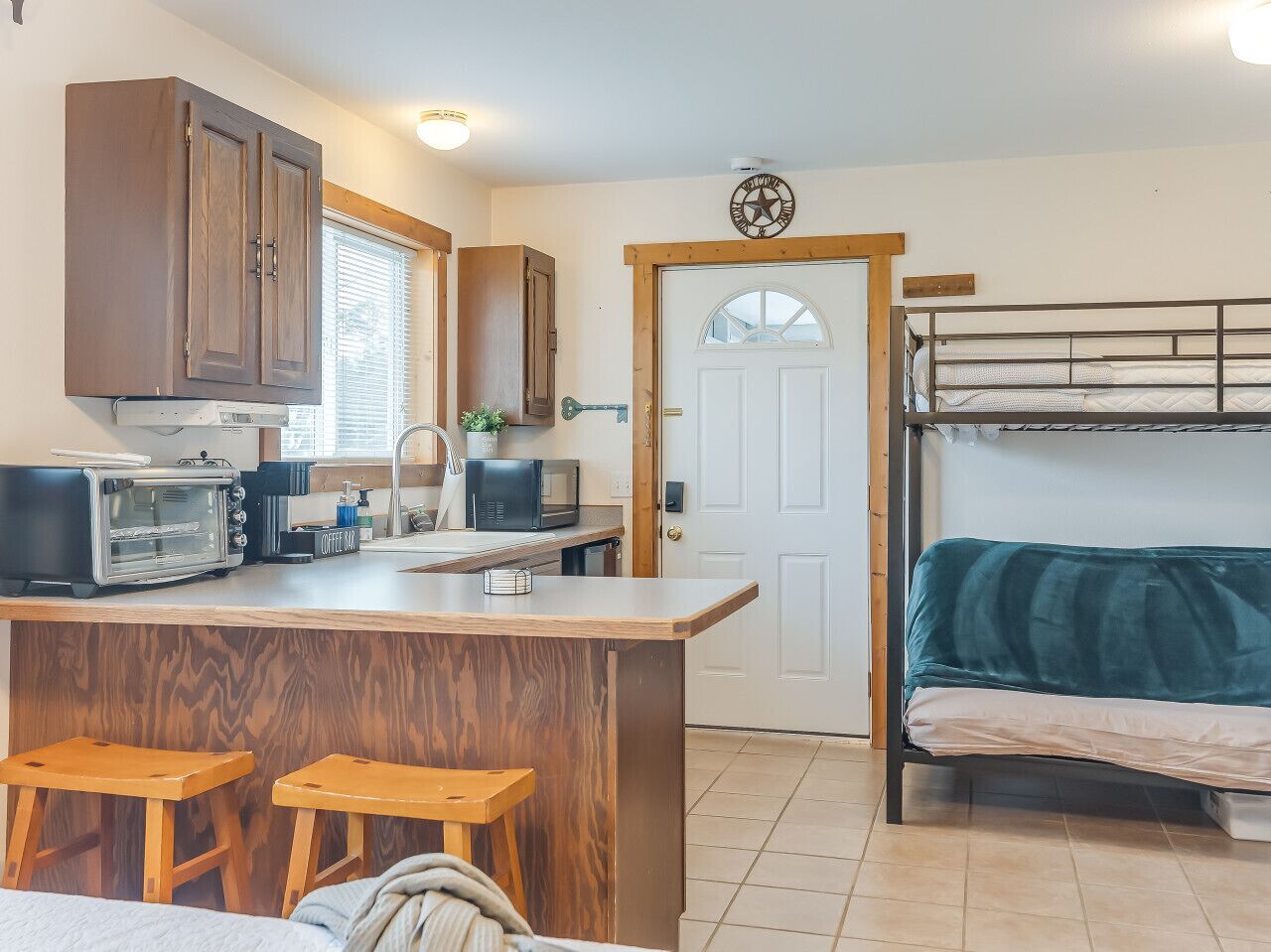 A compact kitchen with a central island, wooden stools, a microwave, a toaster, and a coffee machine.