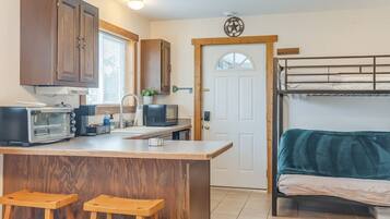 A compact kitchen with a central island, wooden stools, a microwave, a toaster, and a coffee machine.
