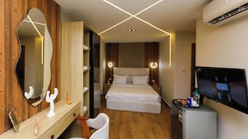 Habitación de hotel con tocador de madera, un espejo grande, cama con ropa de cama blanca, televisor y un refrigerador pequeño.