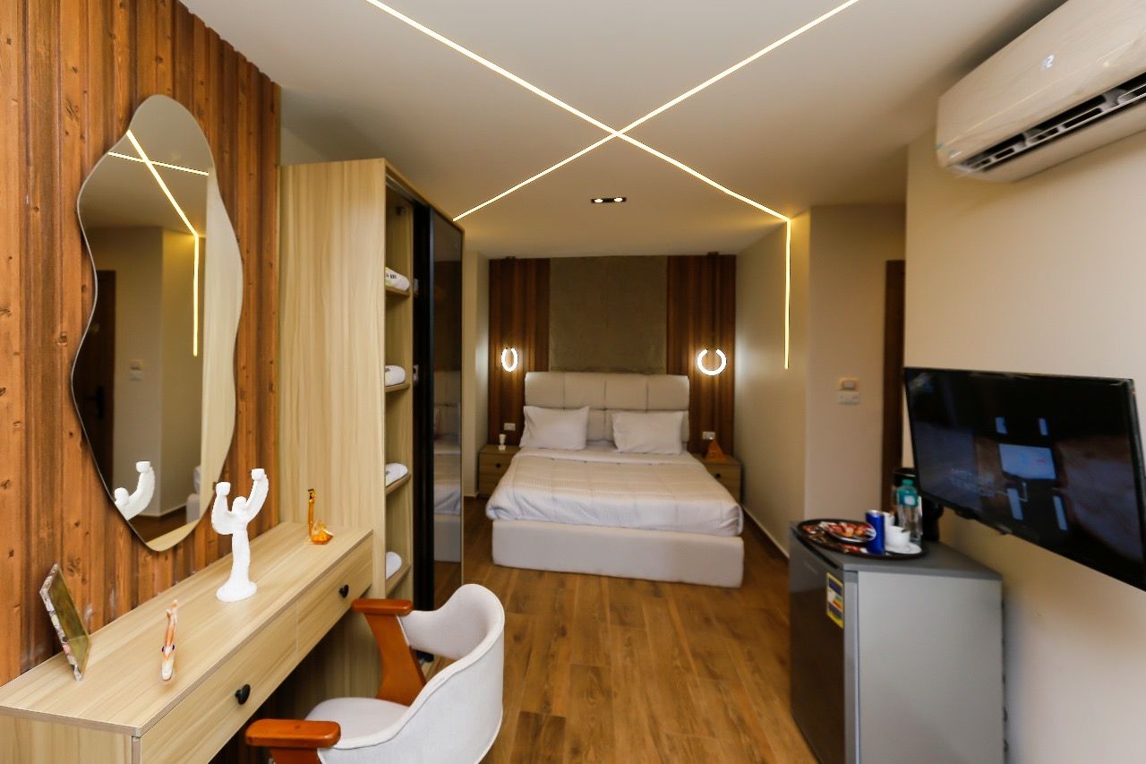 A hotel room with a bed, bedside tables, a mirror, a TV, and an air conditioning unit.