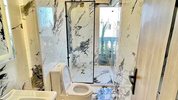 A modern bathroom with a marble floor, a glass shower enclosure, and a toilet.