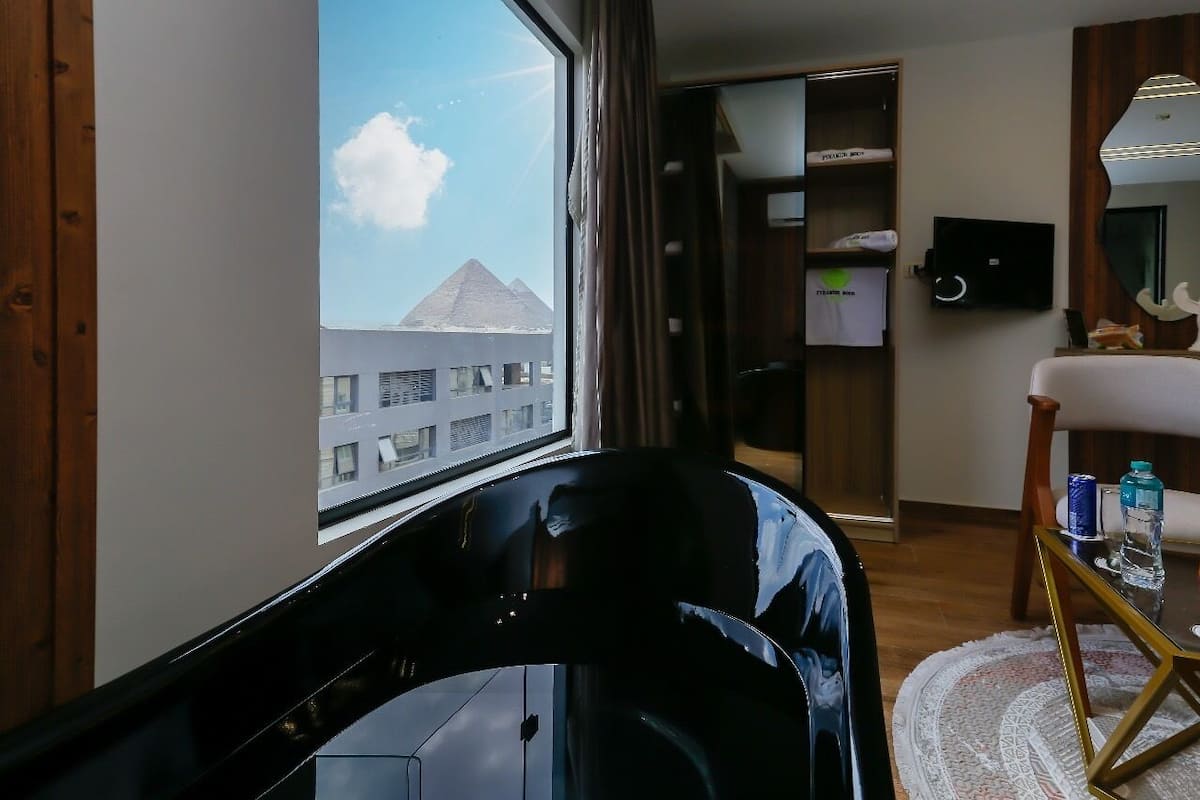 Habitación de hotel con vista a una pirámide, televisión, espejo y una mesa con botellas de agua.
