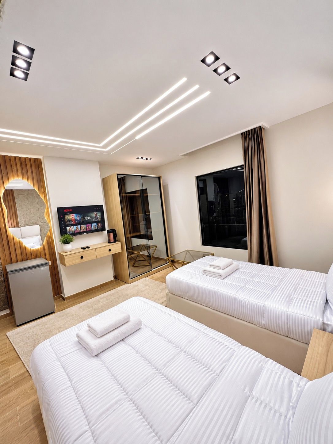 Habitación de hotel con dos camas, televisión, minibar y un ventanal grande.