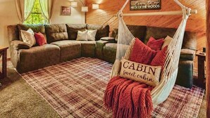 Ein gemütliches Blockhausschlafzimmer mit Holzbalkendecke, einer Couch, einem Hängesessel mit einem Schild und einem karierten Teppich.