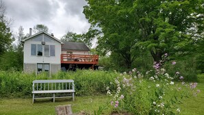 A white house with a red deck, surrounded by greenery and a white bench. - "Pleasant Brook Cottage" near Roxbury Village - Woods, Streams, Wi-fi, sleeps 6 (Roxbury)