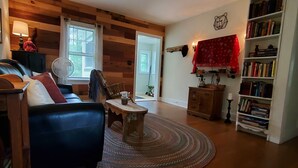 A cozy living room with a wooden ceiling, a leather sofa, a coffee table, a bookshelf, and a red curtain. - "Pleasant Brook Cottage" near Roxbury Village - Woods, Streams, Wi-fi, sleeps 6 (Roxbury)