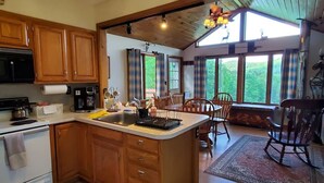 A kitchen with wooden cabinets, a stove, and a dining area with a table and chairs. - "Pleasant Brook Cottage" near Roxbury Village - Woods, Streams, Wi-fi, sleeps 6 (Roxbury)