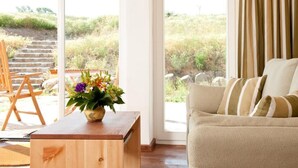 A room with a wooden coffee table, a beige sofa, and a large window offering a view of a garden and steps outside. - Bio- und Gesundheitshotel Gutshaus Parin (Damshagen)
